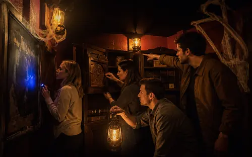 Vier Personen suchen im Escape Room in Oberkirch bei Laternenlicht und mit einer UV-Lampe nach Hinweisen an einer Wand und in einem alten Schrank