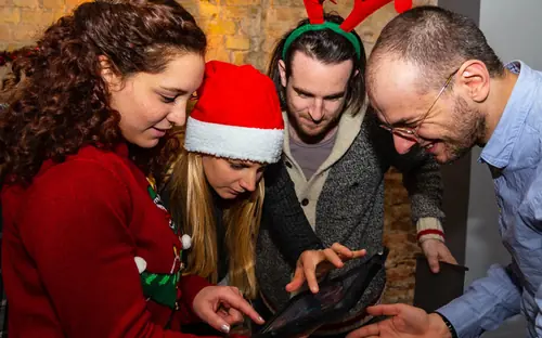 Gruppe mit Weihnachtsmützen löst gemeinsam eine Aufgabe am Tablet beim Weihnachts-Exitgame in Oberkirch