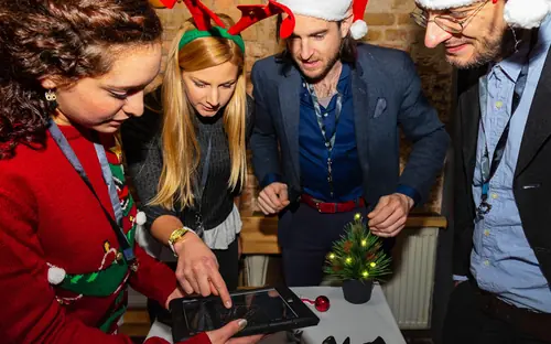 Gruppe mit Weihnachtsmützen löst gemeinsam eine Aufgabe am Tablet beim Weihnachts-Exitgame „Der magische Trank“ in Oberkirch